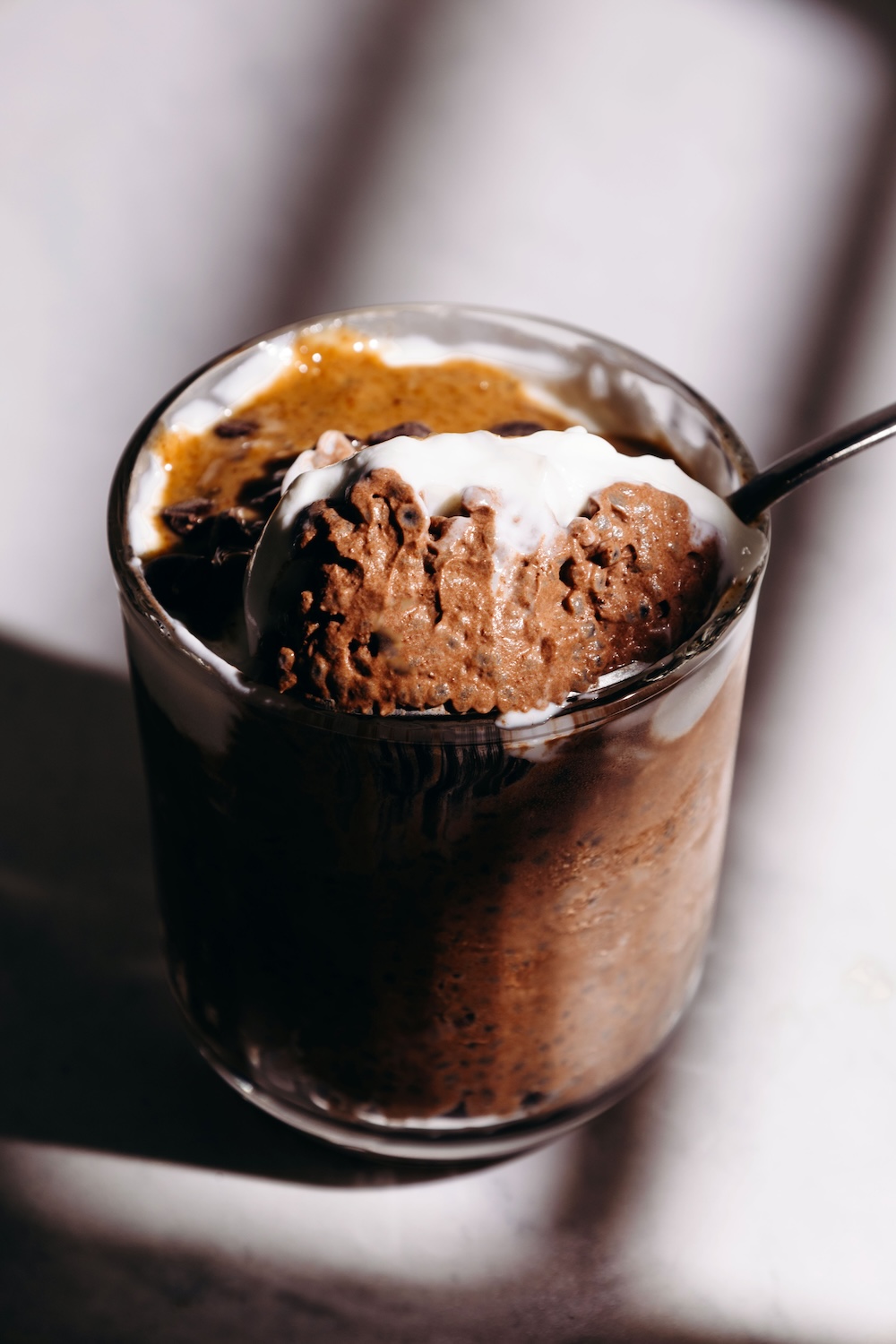 Chocolate basil seed pudding served in a clear glass with yogurt, almond butter drizzle, and dark chocolate chips, with a spoon resting on the rim.