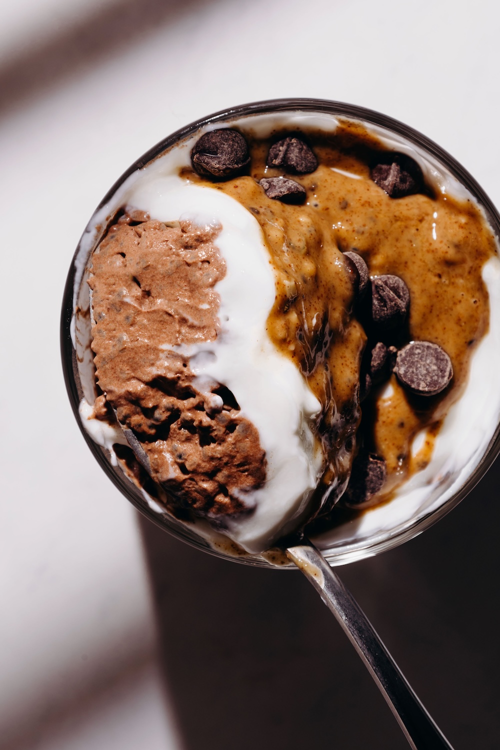 Close-up overhead view of a spoonful of chocolate basil seed pudding topped with yogurt, almond butter, and dark chocolate chips in a glass.
