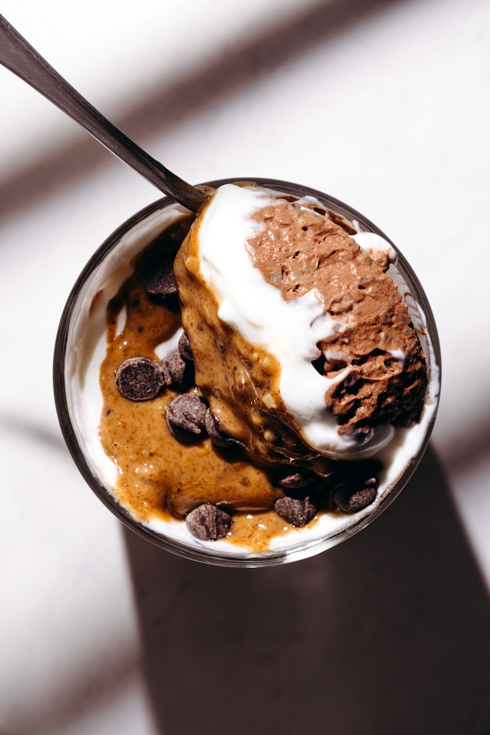 Chocolate basil seed pudding in a glass bowl topped with dairy-free yogurt, almond butter drizzle, and dark chocolate chips, with a spoon lifting a bite.