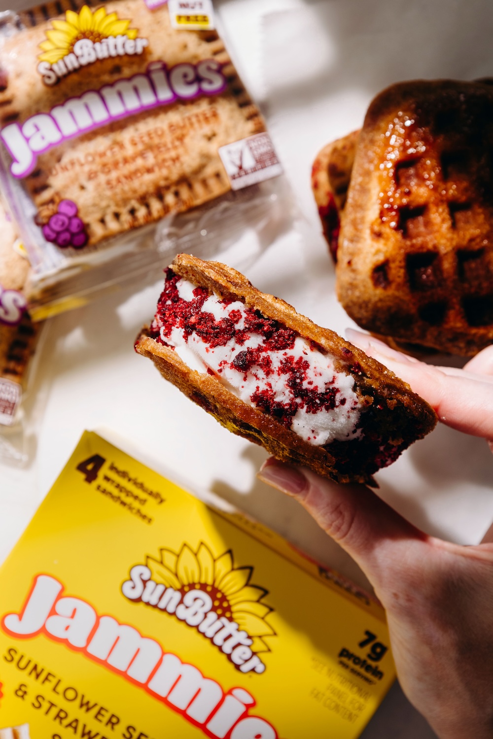 Waffle iron PB&J ice cream sandwich made with SunButter Jammies, filled with dairy-free vanilla ice cream and rolled in freeze-dried grape dust, held up to show the cross section