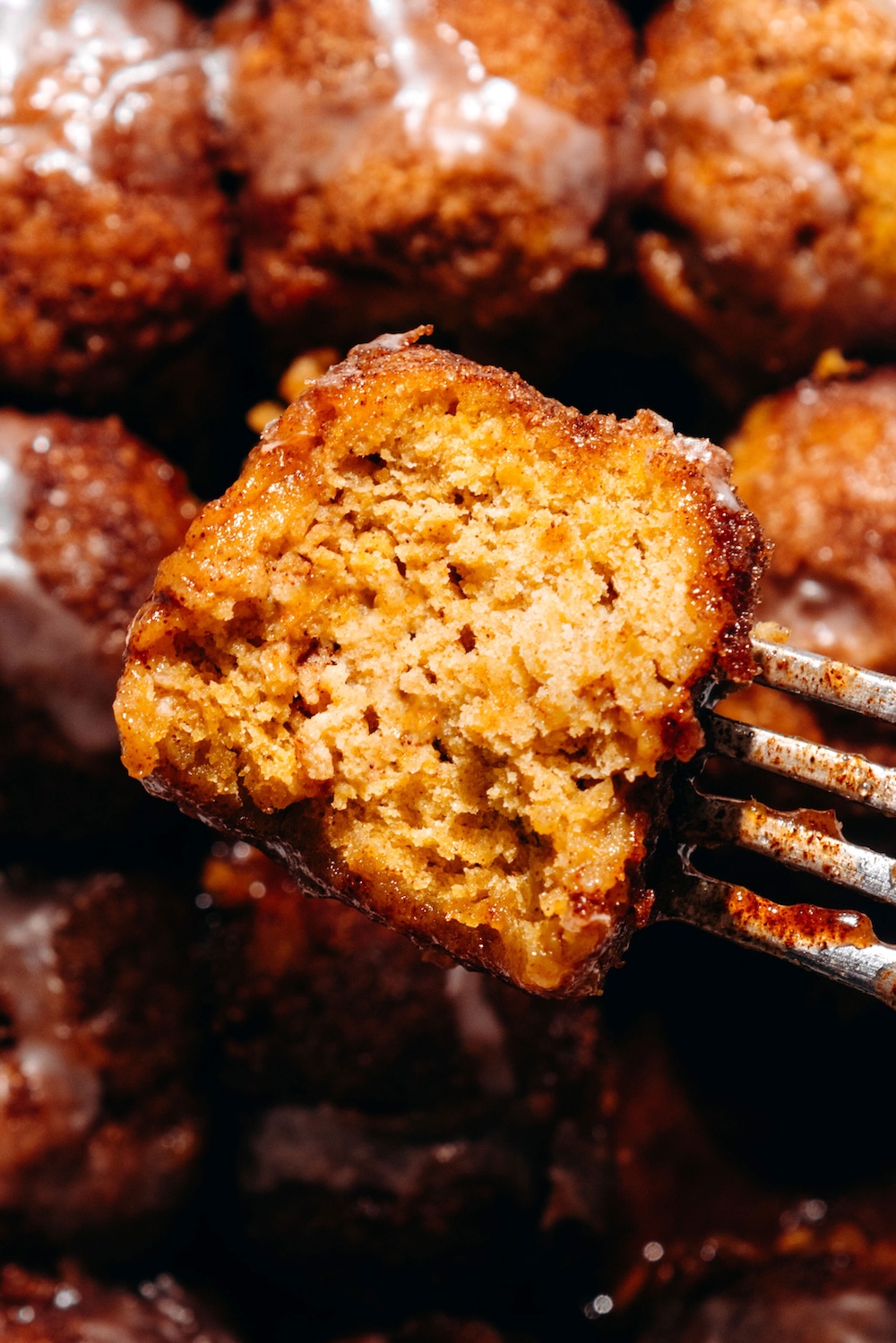 Close-up of a gooey vegan pumpkin cinnamon roll bite on a fork with cinnamon sugar syrup.