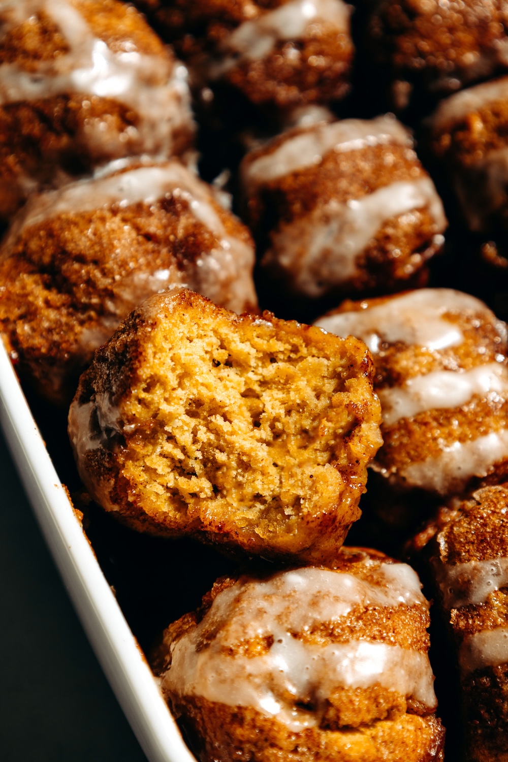 A pumpkin cinnamon roll bite with a bite taken out, showing the soft, fluffy inside.