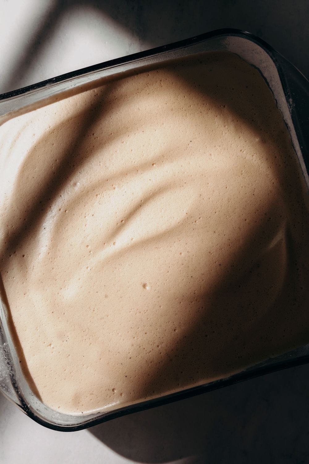 Whipped protein marshmallow mixture spread smoothly in a square glass baking dish before chilling.