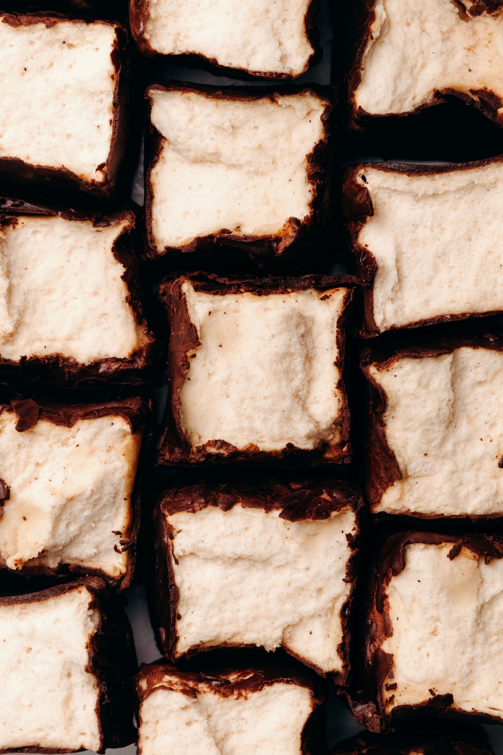 Overhead view of chocolate-coated protein marshmallow squares cut open to show their pillowy centers.