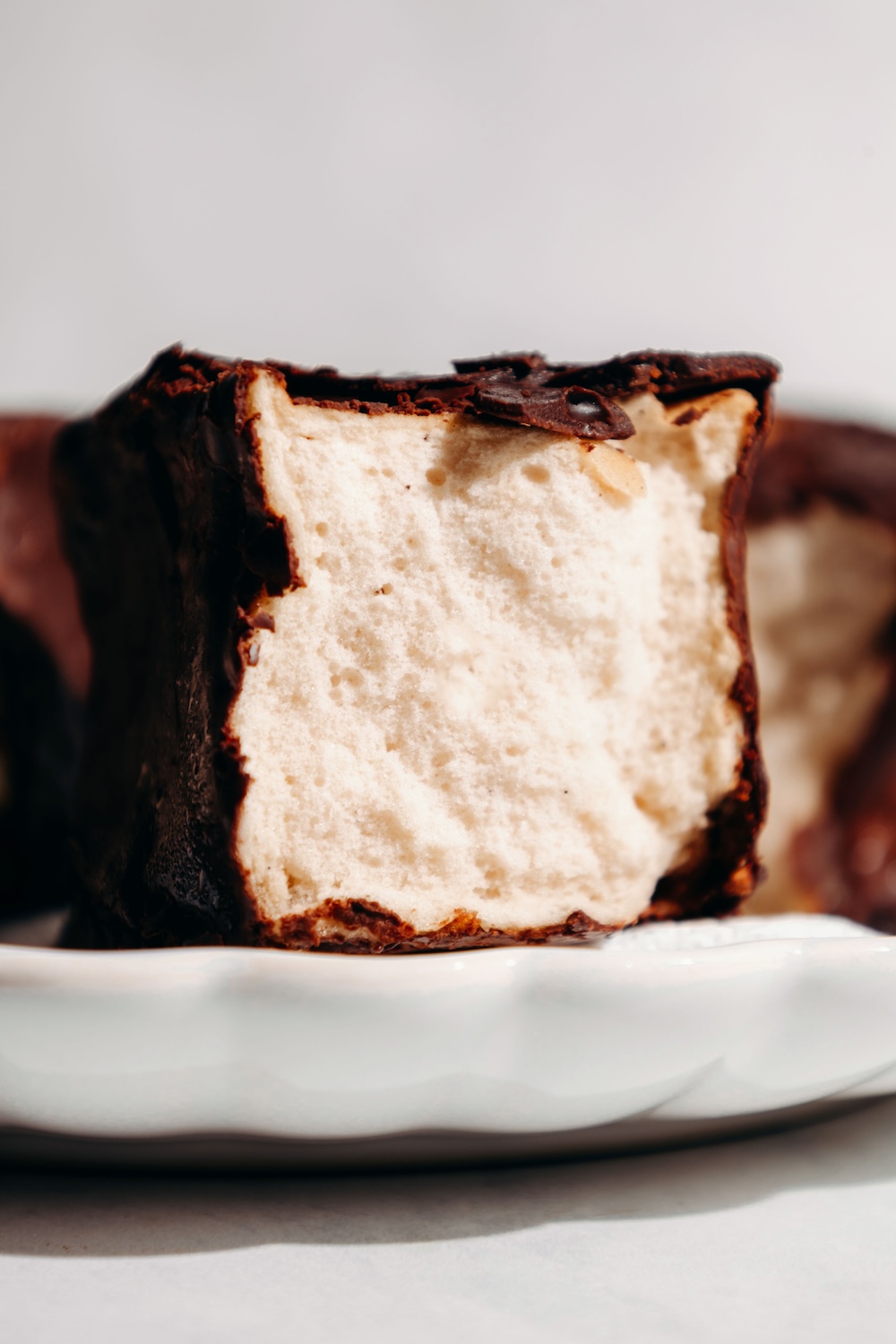Close-up of a chocolate-dipped protein marshmallow sliced open on a white scalloped plate.