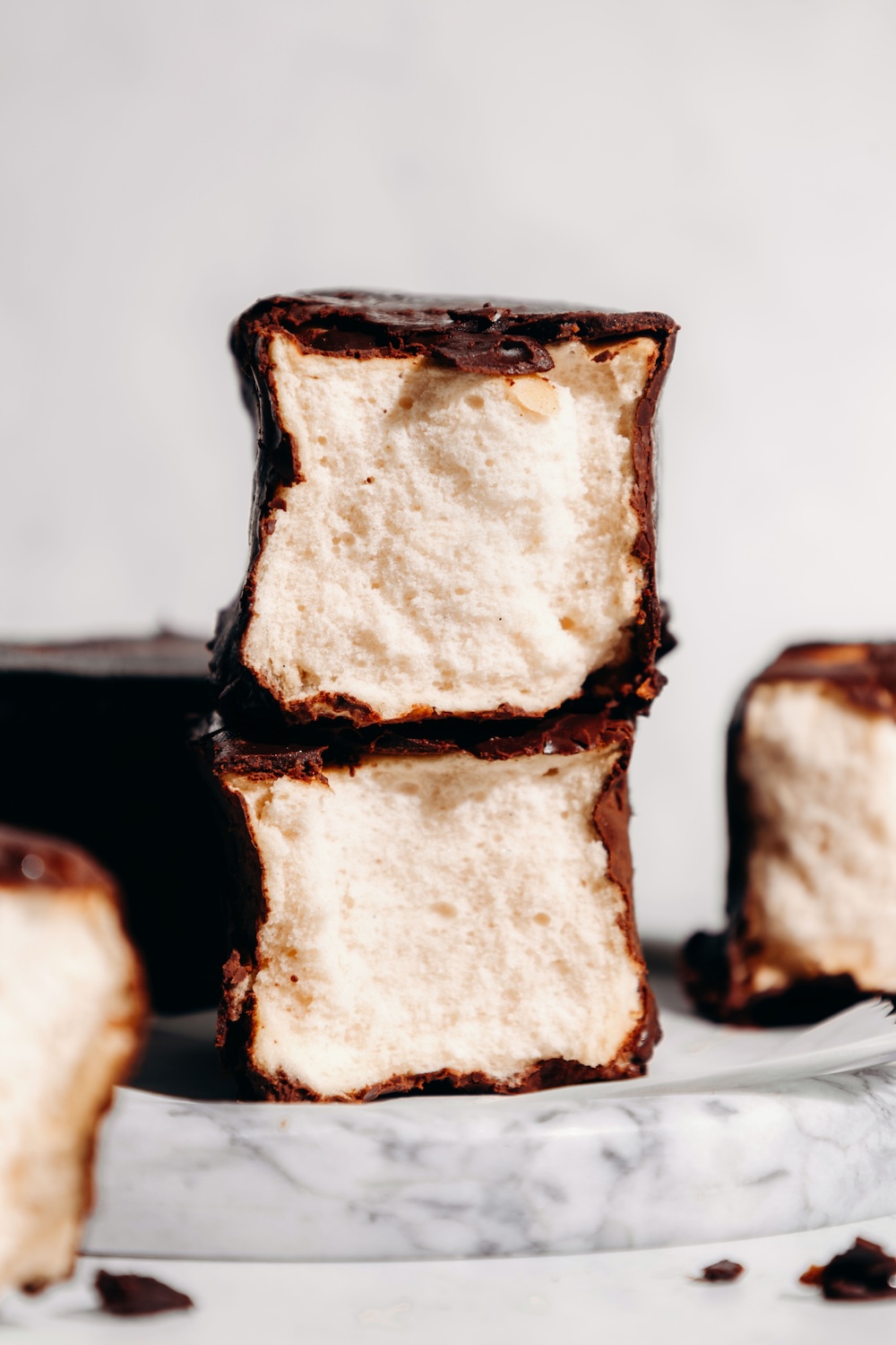 Two chocolate-dipped protein marshmallows stacked on a marble board, showing their soft, fluffy texture.